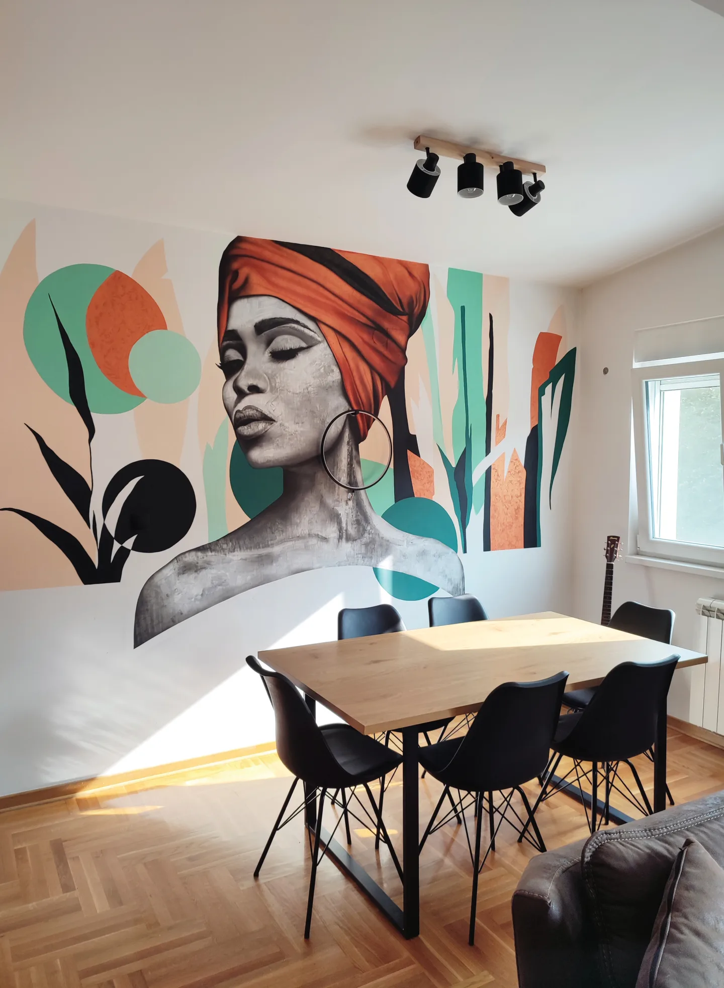 Portrait in an orange headwrap with green shapes above an apartment dining table.