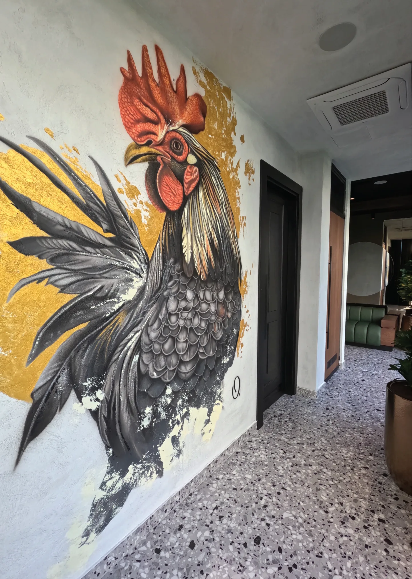 Black rooster mural with a red comb and gold accents along the restaurant wall.