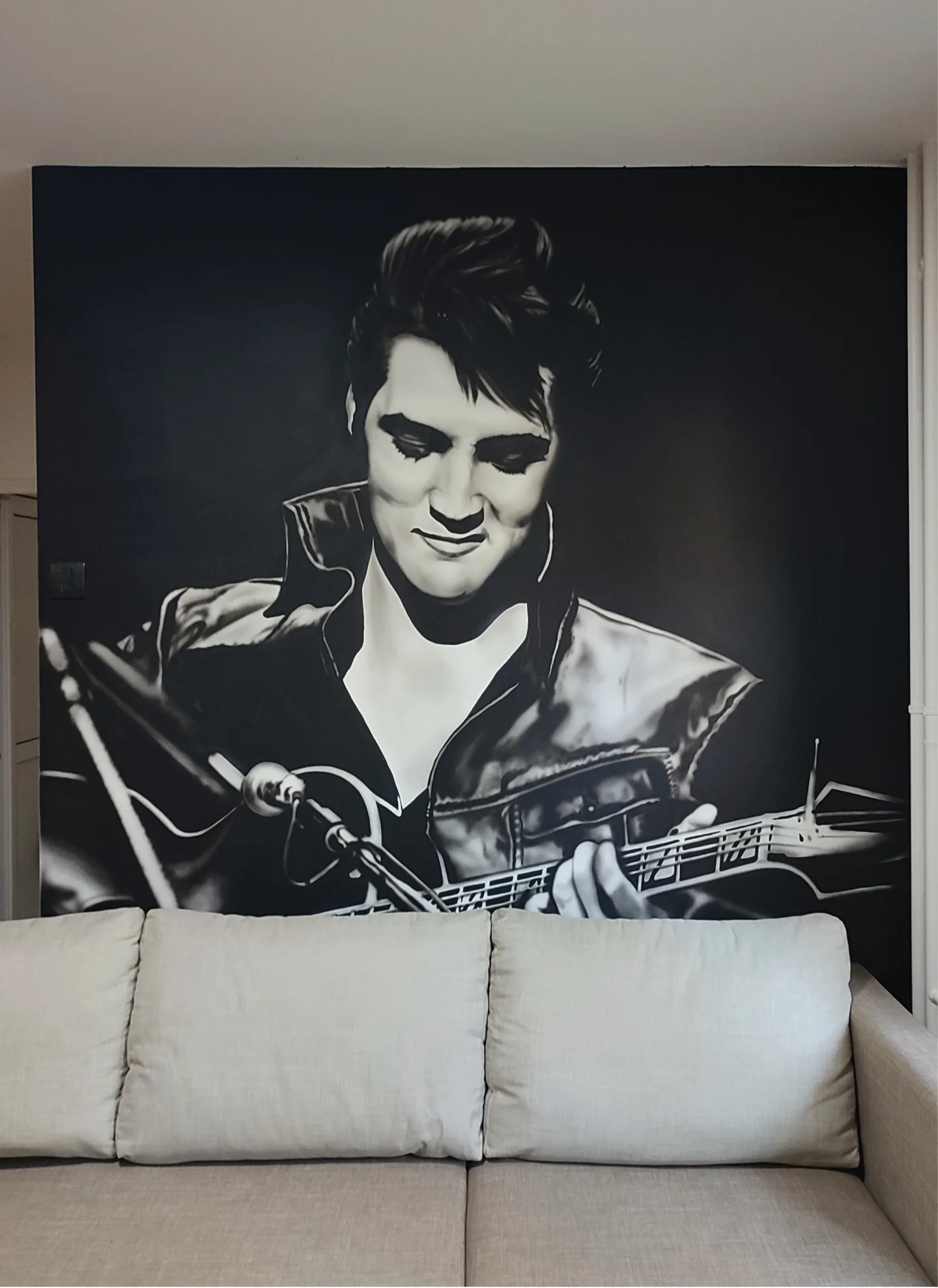 Black and white Elvis Presley mural behind a light-coloured sofa.