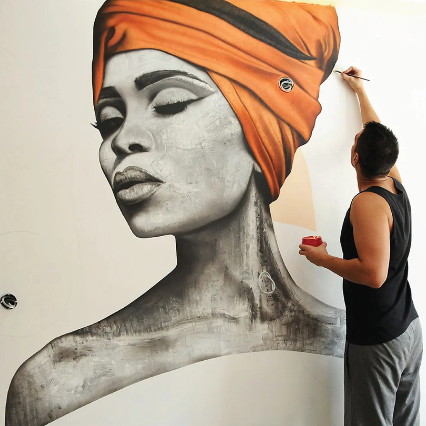 Artist painting a portrait mural with an orange headwrap.