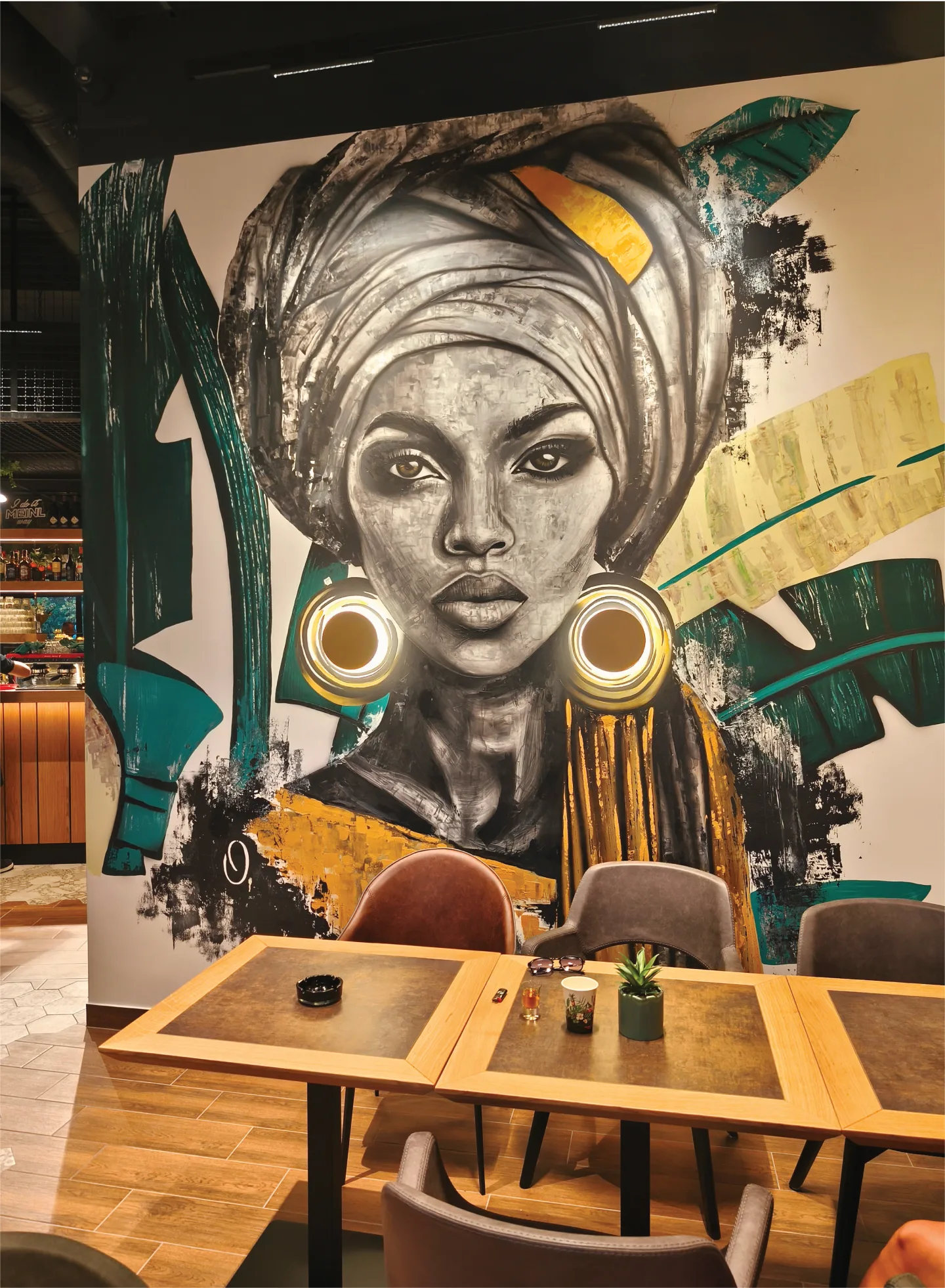 Portrait mural with illuminated circular earrings above café seating at Lady K3.